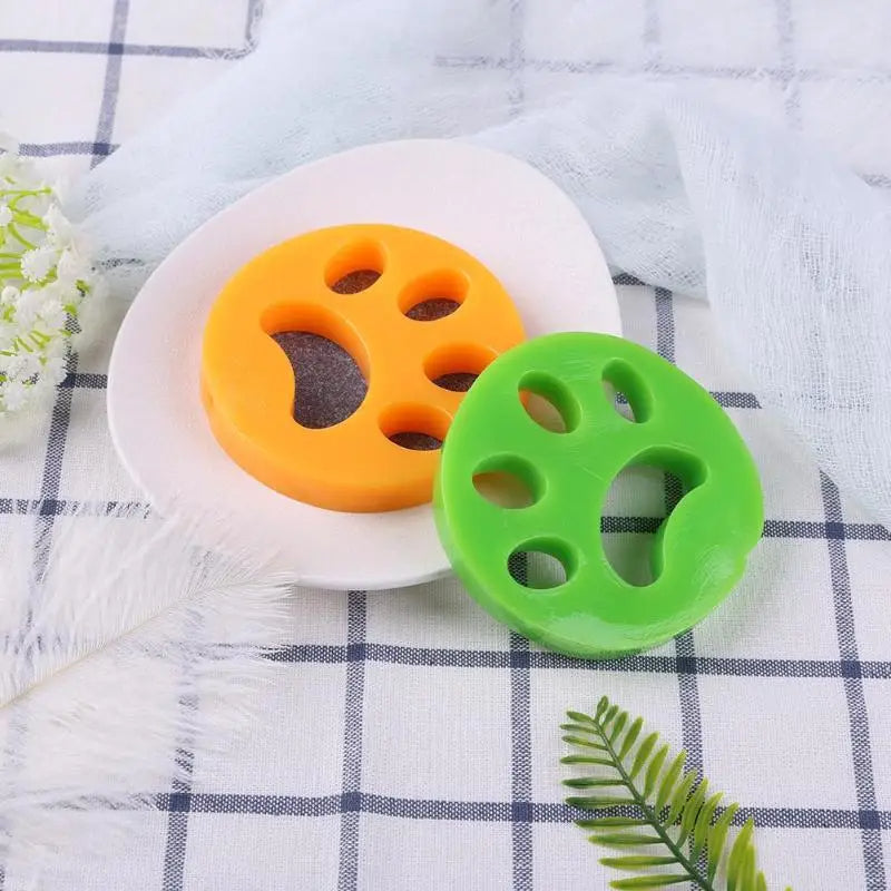 Green and orange paw-shaped reusable pet hair removers displayed on fabric surface